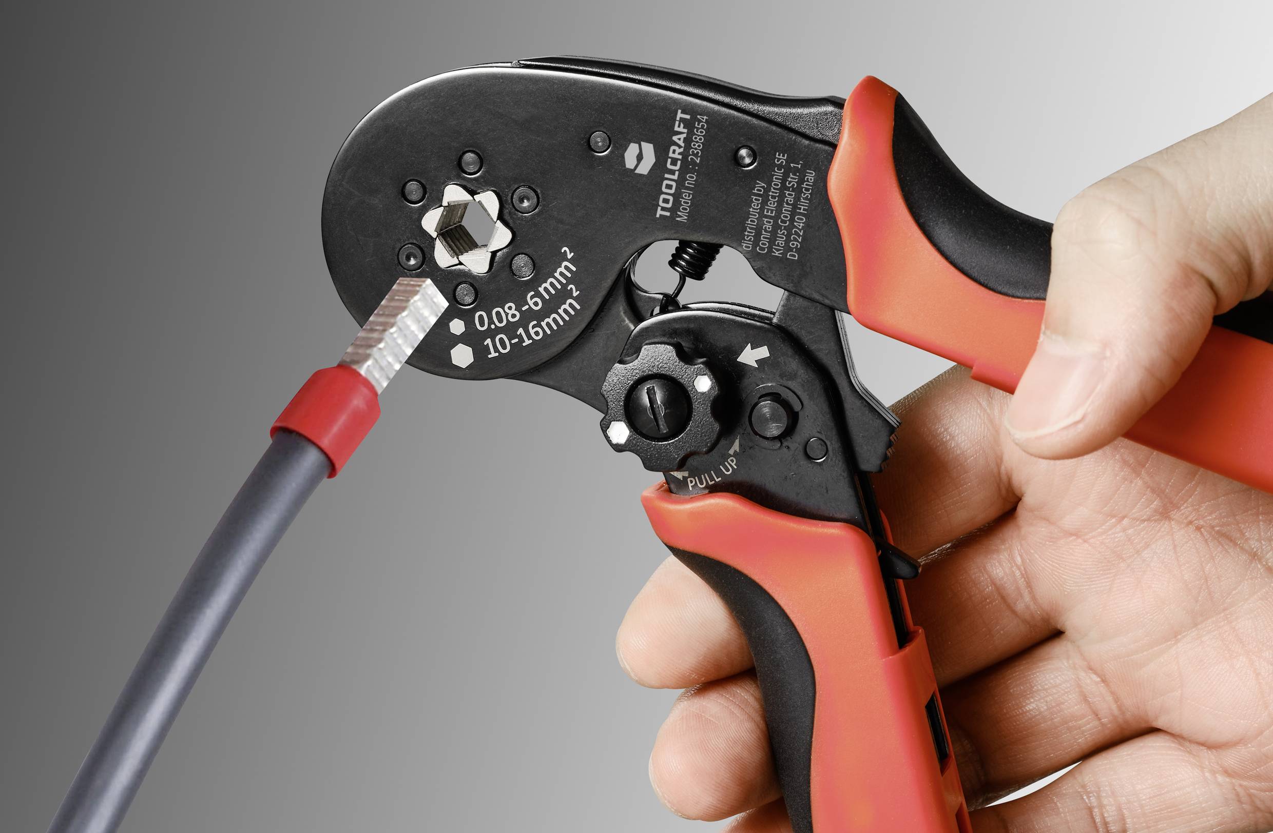 A hand is holding a red crimping pliers about to attach a cable lug to a black cable.