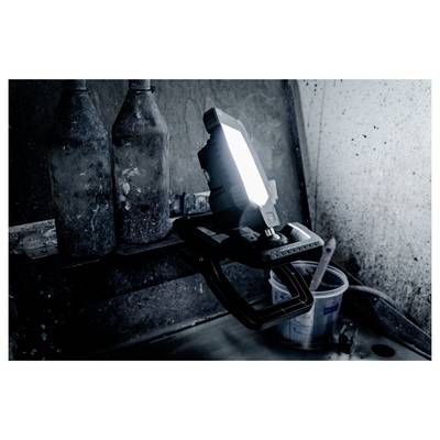 Portable work light on a stand shining in a dark, dusty industrial corner beside a bucket and hose.