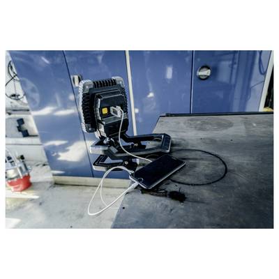 Portable work light on a table with a smartphone connected by cables in an industrial workshop.