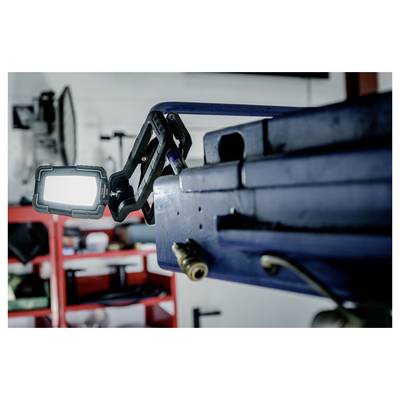 Close-up of a mounted LED work light on a blue machine arm in a workshop, with red shelving blurred in the background.