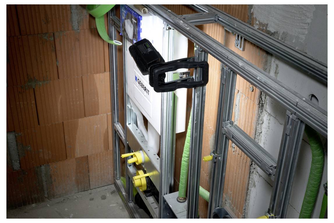 Partially built interior wall framing with metal studs, insulation and green pipes around a recessed mechanical unit with yellow valves.<br>