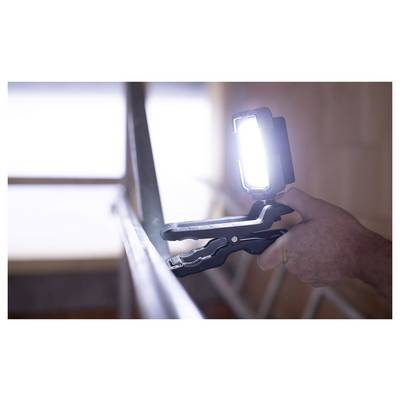 Person using a handheld LED work light clipped to a bracket while working indoors, with bright light aimed at the surface.