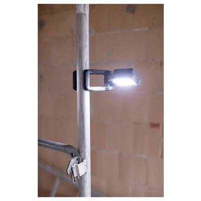 LED work light clamped to a vertical metal pole in an unfinished brick interior, with a second clamp visible below.
