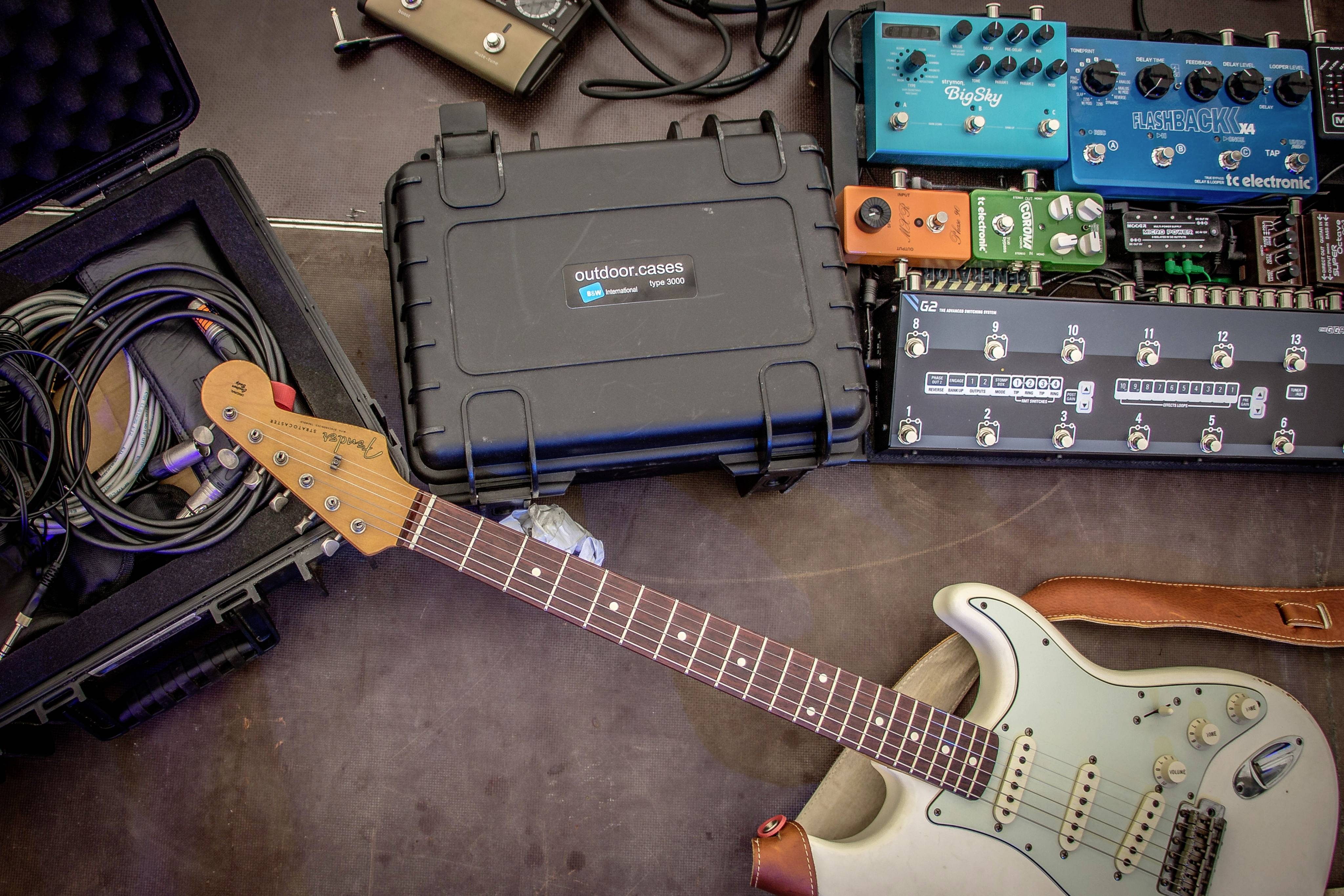 An electric guitar lies beside several effect pedals and cables, prepared for music or stage equipment.