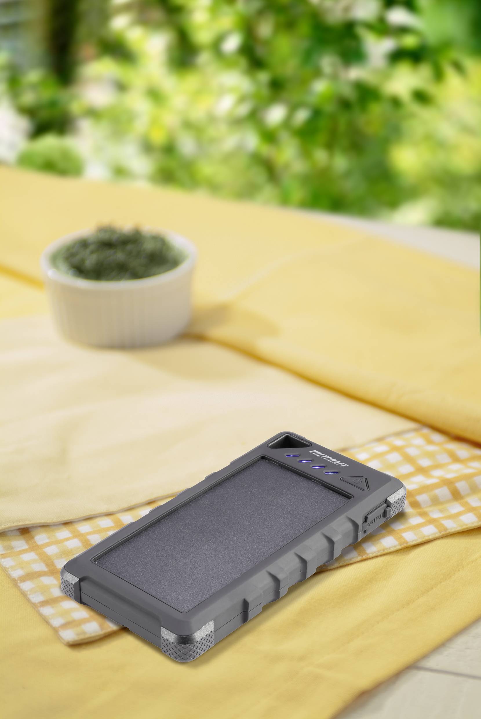 Solar panel charger on a yellow cloth outdoors, surrounded by greenery.