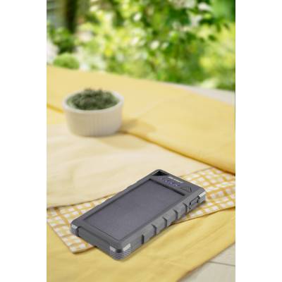 Solar panel charger on a yellow cloth outdoors, surrounded by greenery.