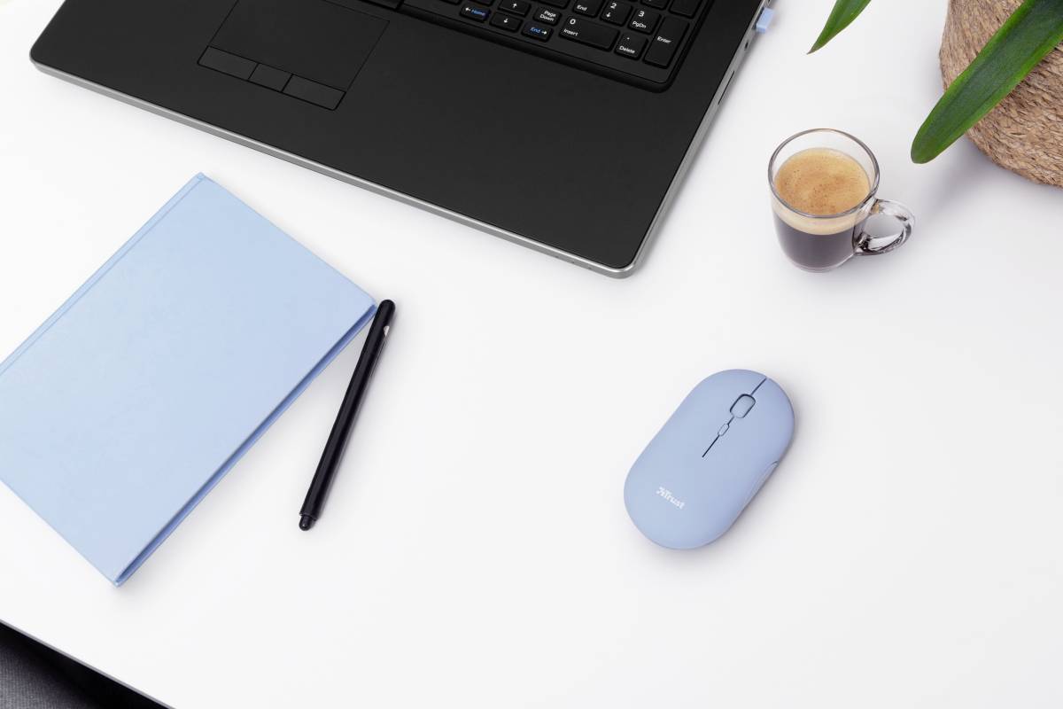 Laptop on a white table, next to a light blue notebook, black pen, blue mouse and a glass of espresso; minimalist arrangement.