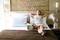 A woman in a white dress is relaxing on a hotel bed. Next to her is a bag and a running humidifier.