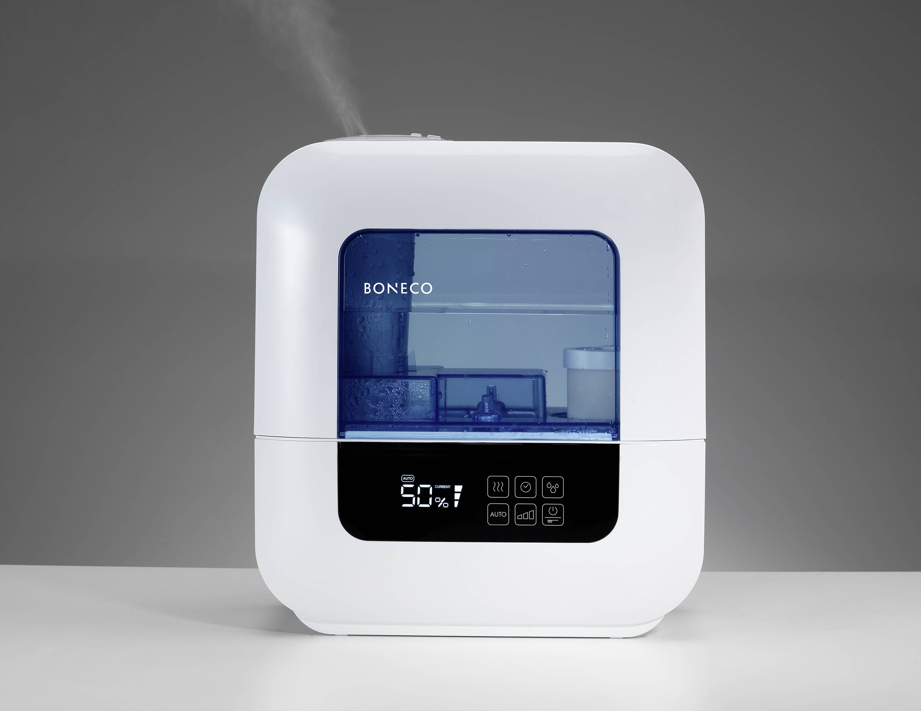 Humidifier in a rectangular, white casing with a digital display. Display shows humidity level of 50%. Device is placed on a table.