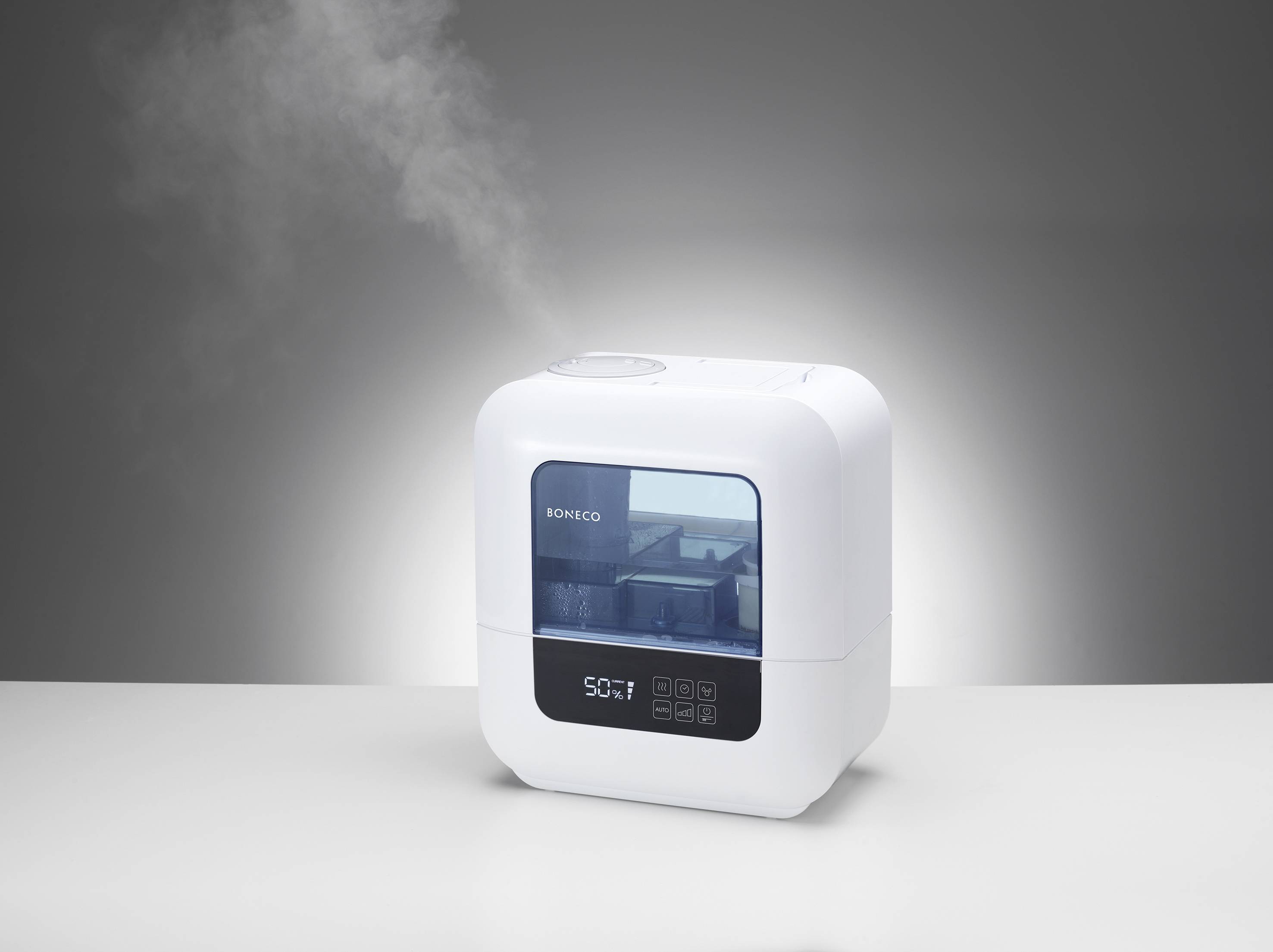 A white air humidifier is sitting on a table and emitting steam. Settings and an indicator are visible on the display.
