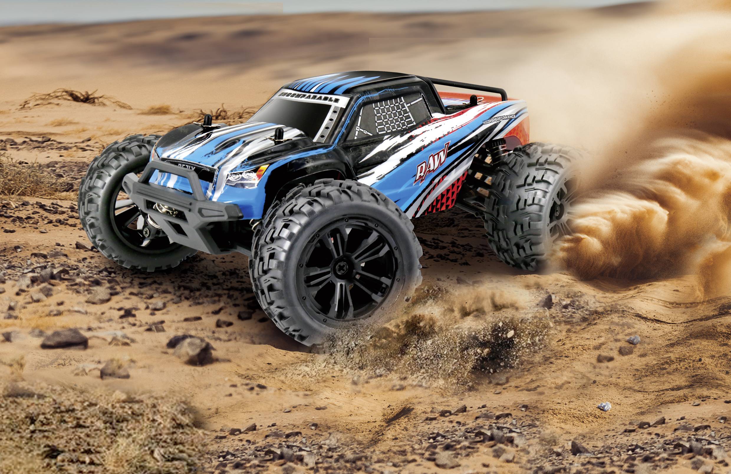 Remote-controlled car in terrain, kicking up dust. The model has blue and red accents and large tyres spinning rapidly.
