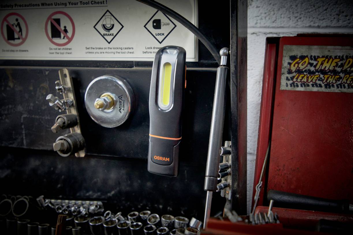 A workshop wall with hooks and clips for tool storage. A torch hangs on a magnet. Tools on the left, a red toolbox on the right.