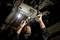 A mechanic is repairing the underside of a vehicle. He is wearing gloves and using tools, while a lamp illuminates the area.