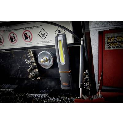 A portable work lamp hangs from a metallic surface in a workshop, surrounded by tools and safety instructions.
