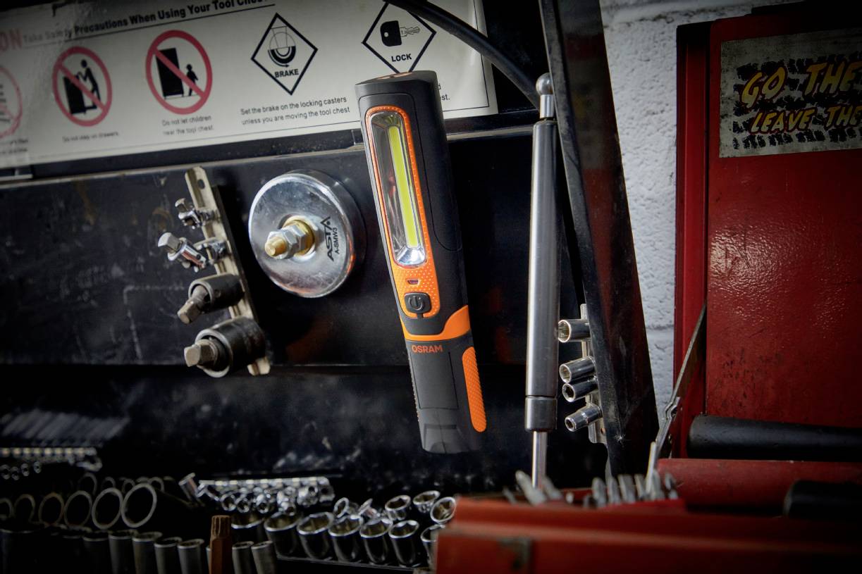 An orange and black screwdriver hangs on a tool wall in a workshop. Nearby, other tools and instructions are visible.