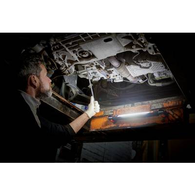 A mechanic inspects the underside of a vehicle in a workshop. He is using a torch for better visibility.