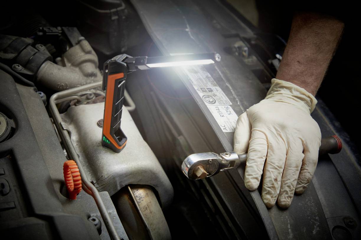 A person wearing gloves is repairing an engine in a car. A bright work lamp illuminates the area.