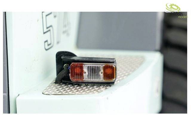 A rear light is situated on a textured metal surface of a light blue vehicle.