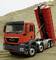 A red lorry with a tilted cargo bed is parked on a sand mound in a construction site scene.