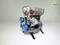 A model of an engine with visible blue pulleys and silver cylinders, displayed against a white background.