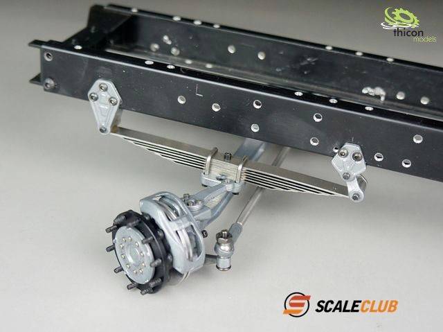 'Model chassis frame with leaf spring suspension and drum brake, illustrated beneath a black metal frame.'