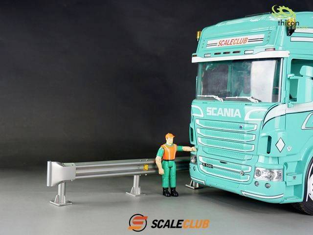Toy lorry in turquoise with 'SCALECLUB' on the windscreen. A figure in an orange-green uniform stands beside it.