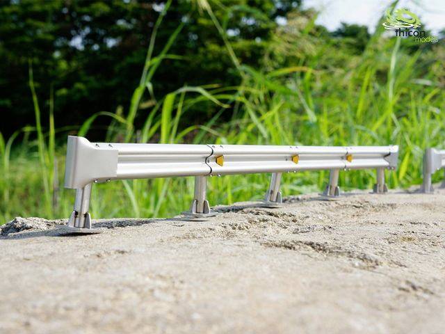 Metal railing on a rock, with green grass and trees in the background.