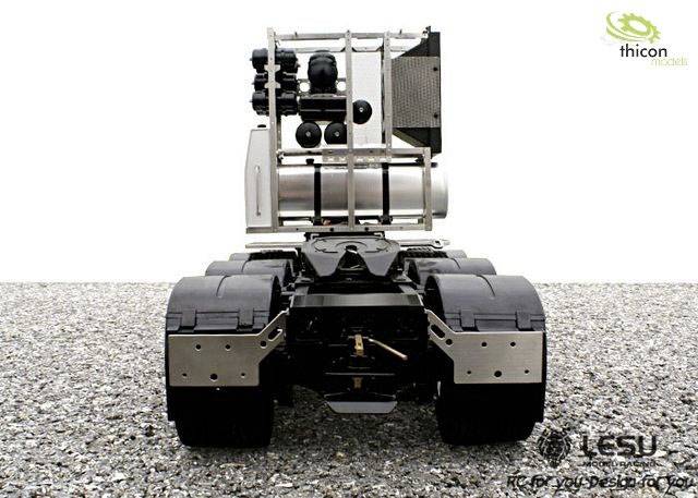 A model vehicle without bodywork displays its mechanical components. It is positioned on a gravel surface, with a logo in the corner.