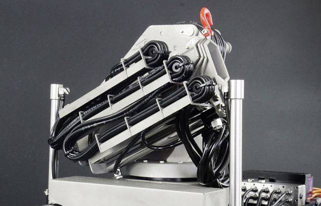 A technical device with multiple stacks of cables, secured to a metal structure and featuring a red handle at the top, against a black background.