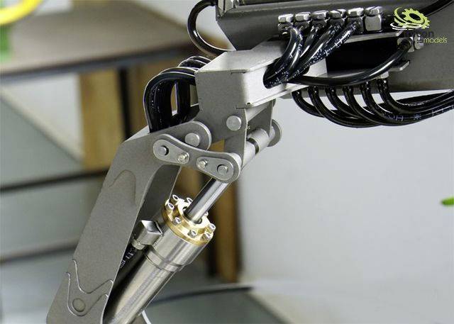 A metallic industrial robotic arm with multiple cables, mounted on a table. It displays technical details and mechanical components.