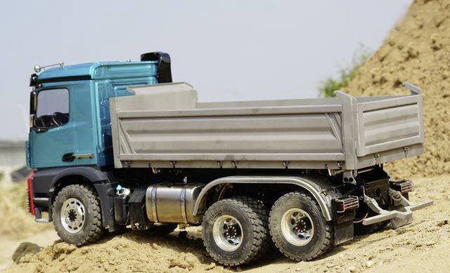 A blue lorry is tipping sand onto a building site. The sky is clear, and no workers are visible.