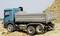 A blue lorry is tipping sand onto a building site. The sky is clear, and no workers are visible.