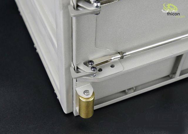 Close-up of a grey metal box with a small gold-coloured metal part on the side. A logo is visible in the top right corner.