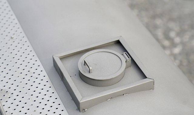 A circular, metallic lid with a handle resting on a perforated metal surface.