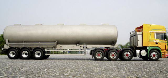 A yellow tanker lorry on a grey road. It has six wheels on the tractor unit and three on the trailer. Clear, bright surroundings.
