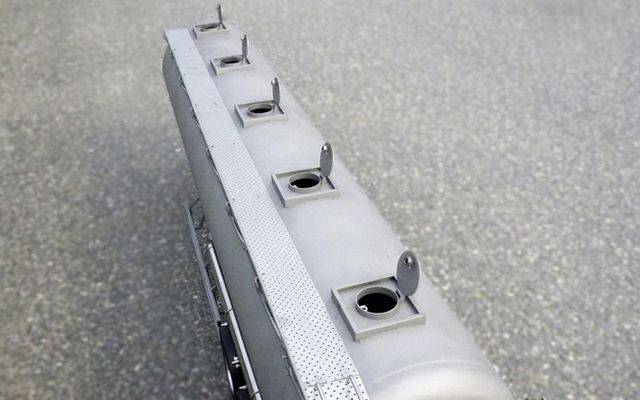 A light grey rectangular metal object with rectangular openings and small flaps, placed on a grey background.