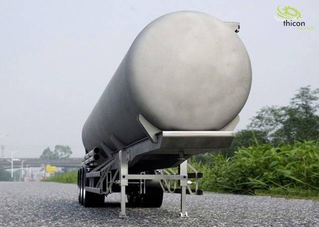 A silver tanker trailer is parked on a road. Trees and a cloudy sky can be seen in the background.