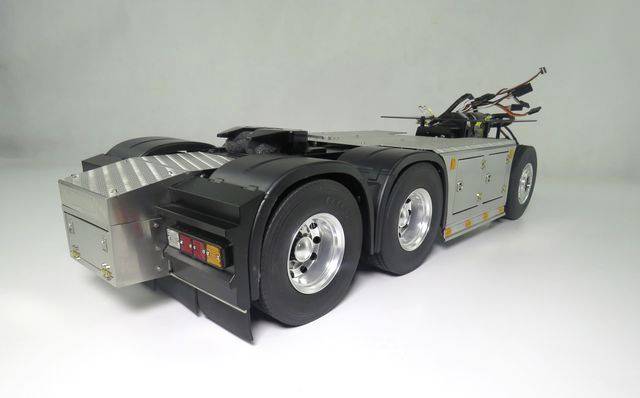A silver model of a heavy-duty lorry chassis with six wheels and wiring on the top, against a white background.