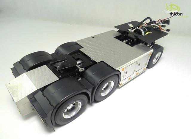 A model of a six-wheeled lorry with metallic surfaces and cables on a white surface.