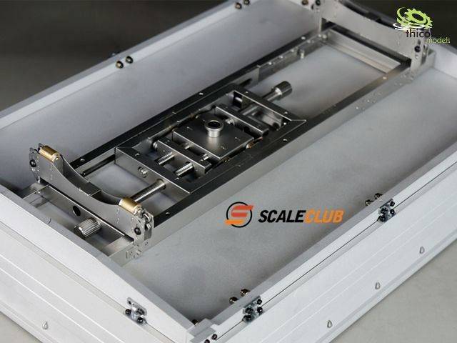 A silver model part in a rectangular frame on a grey background, with the 'SCALECLUB' logo in the centre, demonstrates precision mechanics.