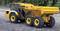 A yellow dump truck with the inscription 'Aoue AT61N' is parked on a gravel surface. The background is blurred with trees.