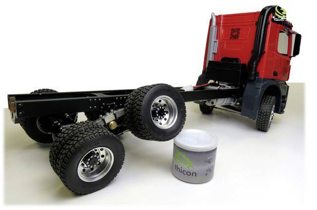 Lorry chassis in model scale with four rear wheels and a red driver's cab. Beside it stands a round container.