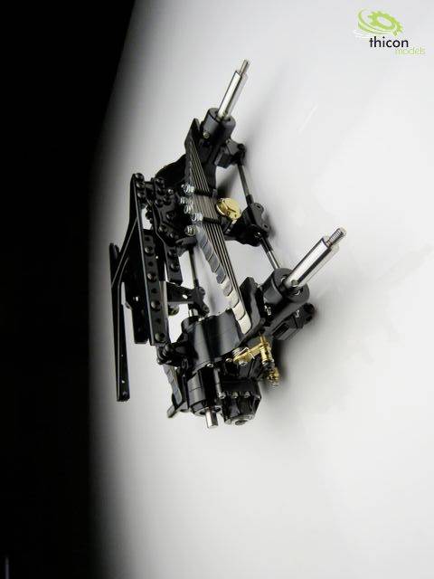 Model of a mechanical chassis with metal and plastic components, suspended against a white background wall.