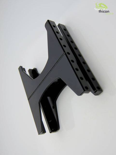 A black, industrial metal component with mounting holes is affixed to a white surface.