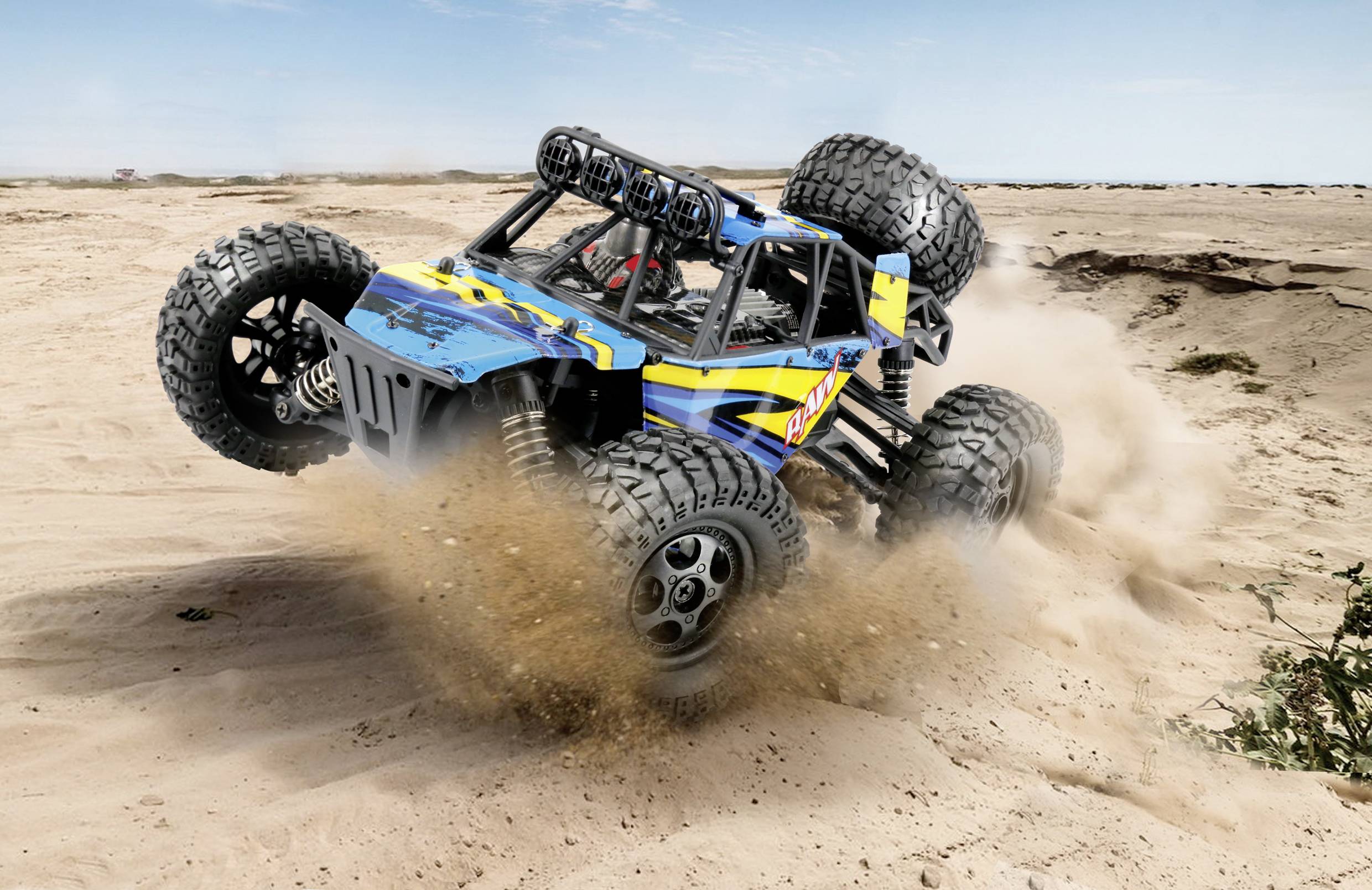 A blue off-road vehicle is driving at high speed through a sandy desert landscape. Dust billows up beneath its large tyres.