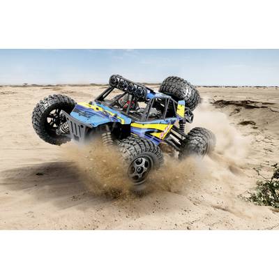 A blue off-road vehicle is driving at high speed through a sandy desert landscape. Dust billows up beneath its large tyres.