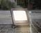 A waterproof, square spotlight shines brightly on a wet, rainy street.