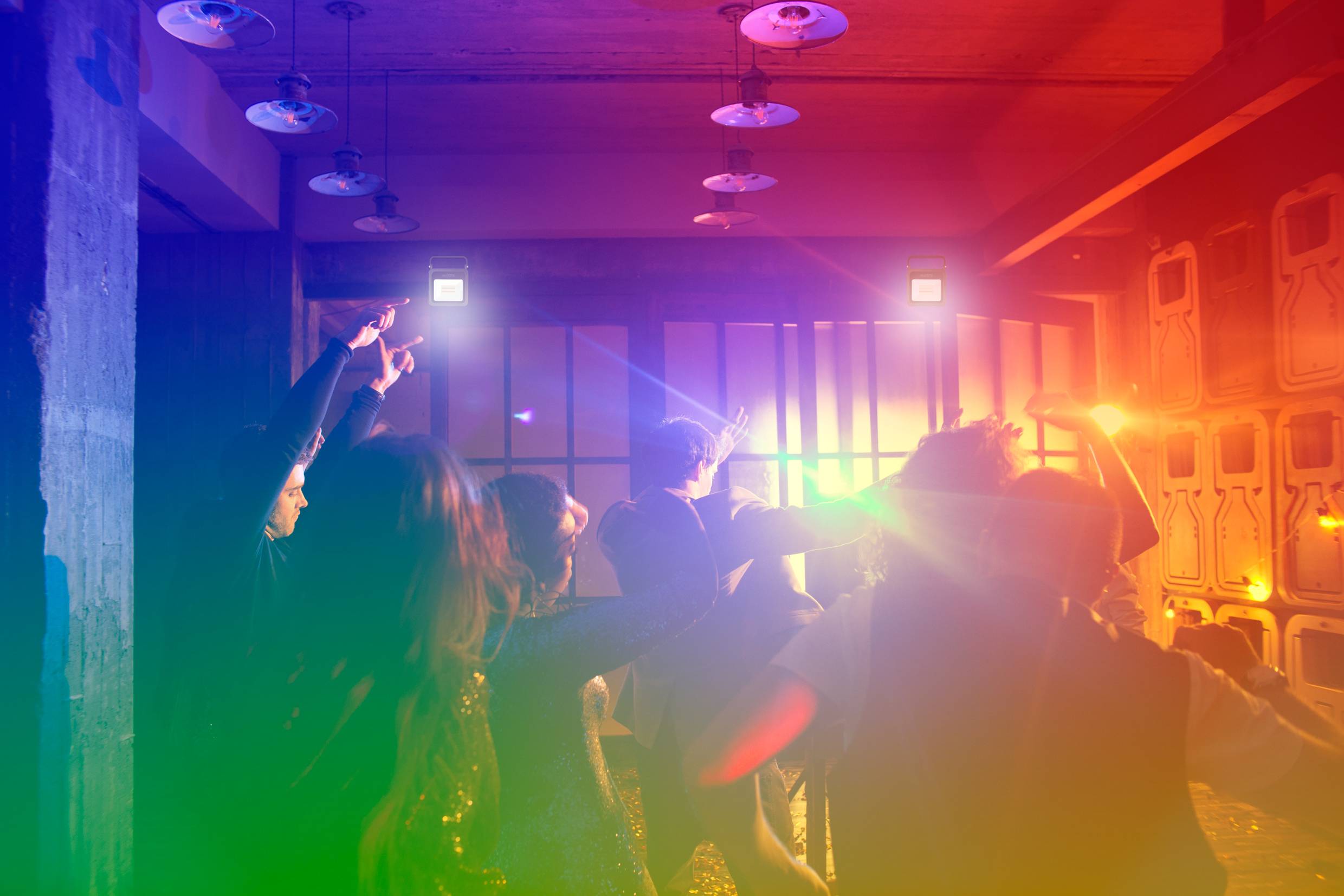 People are dancing in a room with colourful lighting. The atmosphere is lively and celebratory. The walls are designed in a modern style.
