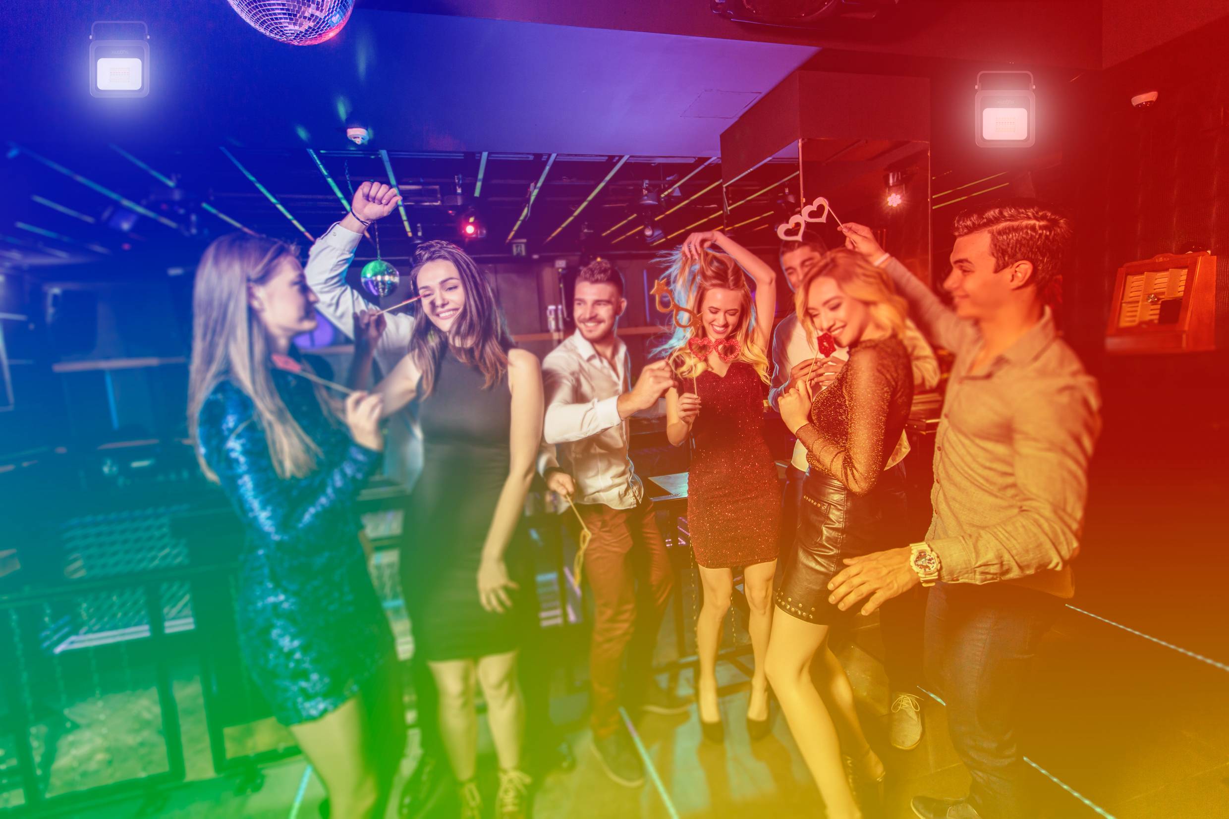 A group of people are dancing and celebrating in a club, surrounded by colourful lights that create a lively and exuberant atmosphere.