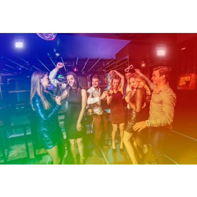 A group of people are dancing and celebrating in a club, surrounded by colourful lights that create a lively and exuberant atmosphere.